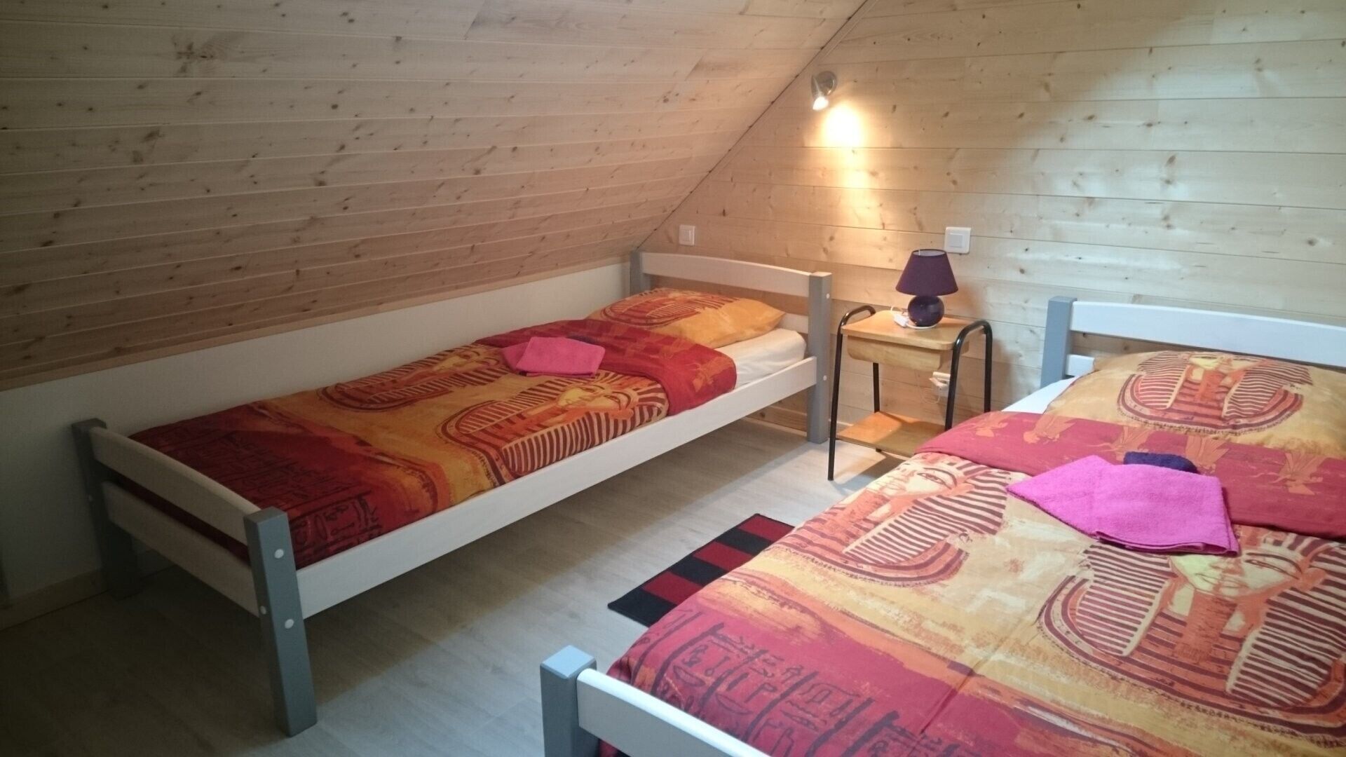 A small, single-room attic bedroom with two bunk beds, a nightstand, and a lamp.