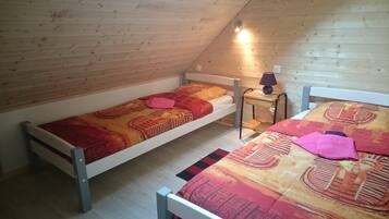A small, single-room attic bedroom with two bunk beds, a nightstand, and a lamp.