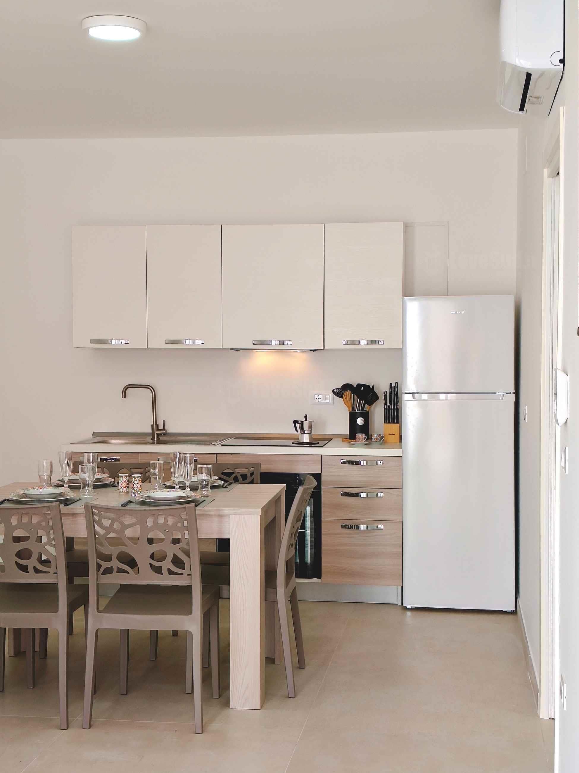 Una cocina moderna con armarios blancos, un refrigerador de acero inoxidable y un comedor con una mesa y sillas.