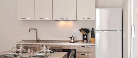 Una cocina moderna con armarios blancos, un refrigerador de acero inoxidable y un comedor con una mesa y sillas.
