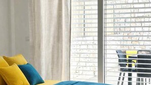 Un dormitorio con una cama, almohadas amarillas y azules, una colcha azul y vistas a un balcón con una silla y una mesa.
