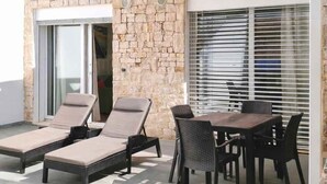 Una terraza en la azotea con muros de piedra, una zona de estar cubierta y una mesa con sillas.