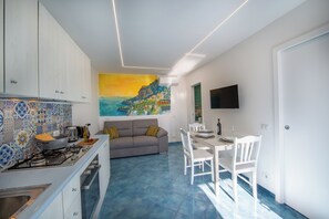 Eine moderne Küche mit Gasherd, ein Essbereich mit Tisch und Stühlen sowie ein Wohnzimmer mit Sofa und einem Bild an der Wand.
