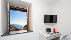 Een kamer met een bureau, een stoel, een aan de muur bevestigde televisie en een raam met uitzicht op de oceaan.