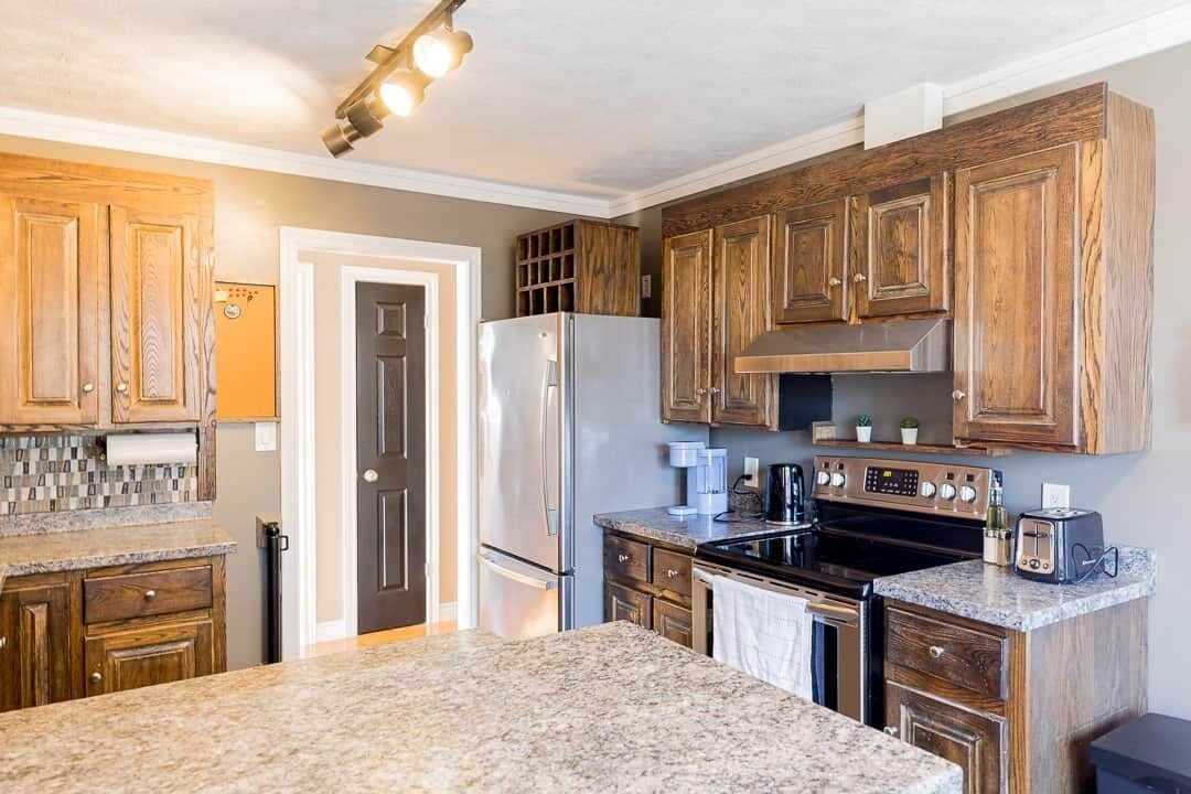 A kitchen with wooden cabinets, a stainless steel refrigerator, a stove, and granite countertops.