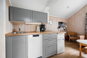 A compact kitchen with grey cabinets, a dishwasher, a coffee maker, and a wicker chair.