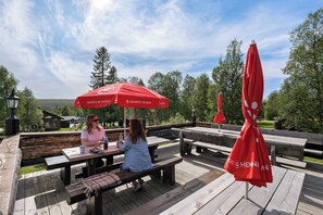Terraza de madera al aire libre con mesas de picnic y sombrillas rojas con el rótulo "HENNIG-OLSEN".