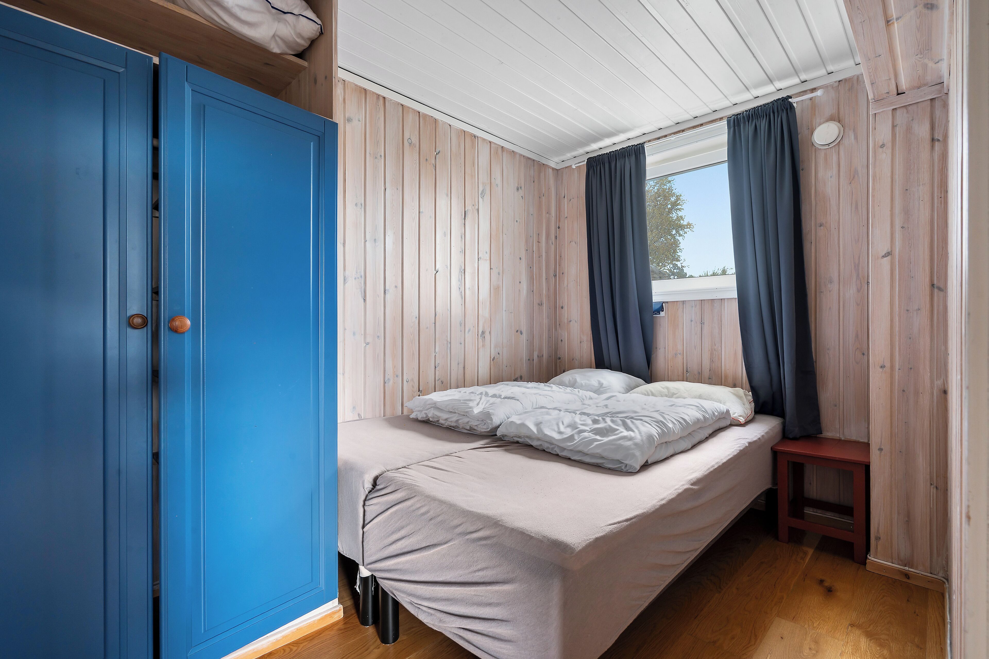 A room with a bed, a blue wardrobe, and a window with curtains.