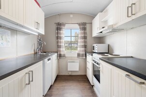 Una cocina compacta con armarios blancos, un microondas y un ventanal con cortinas a cuadros.
