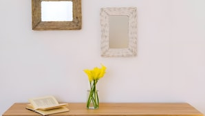 Ein Holztisch mit einem Buch und einer Vase voller gelber Blumen.