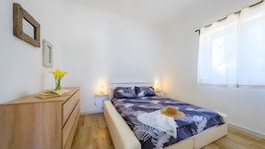 Ein Schlafzimmer mit einem Bett, Nachttischlampen, einer Holzkommode und einem Fenster mit Vorhängen.