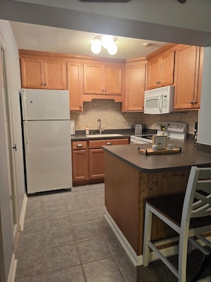 A kitchen with wooden cabinets, a white refrigerator, a microwave, a stove, and a sink.