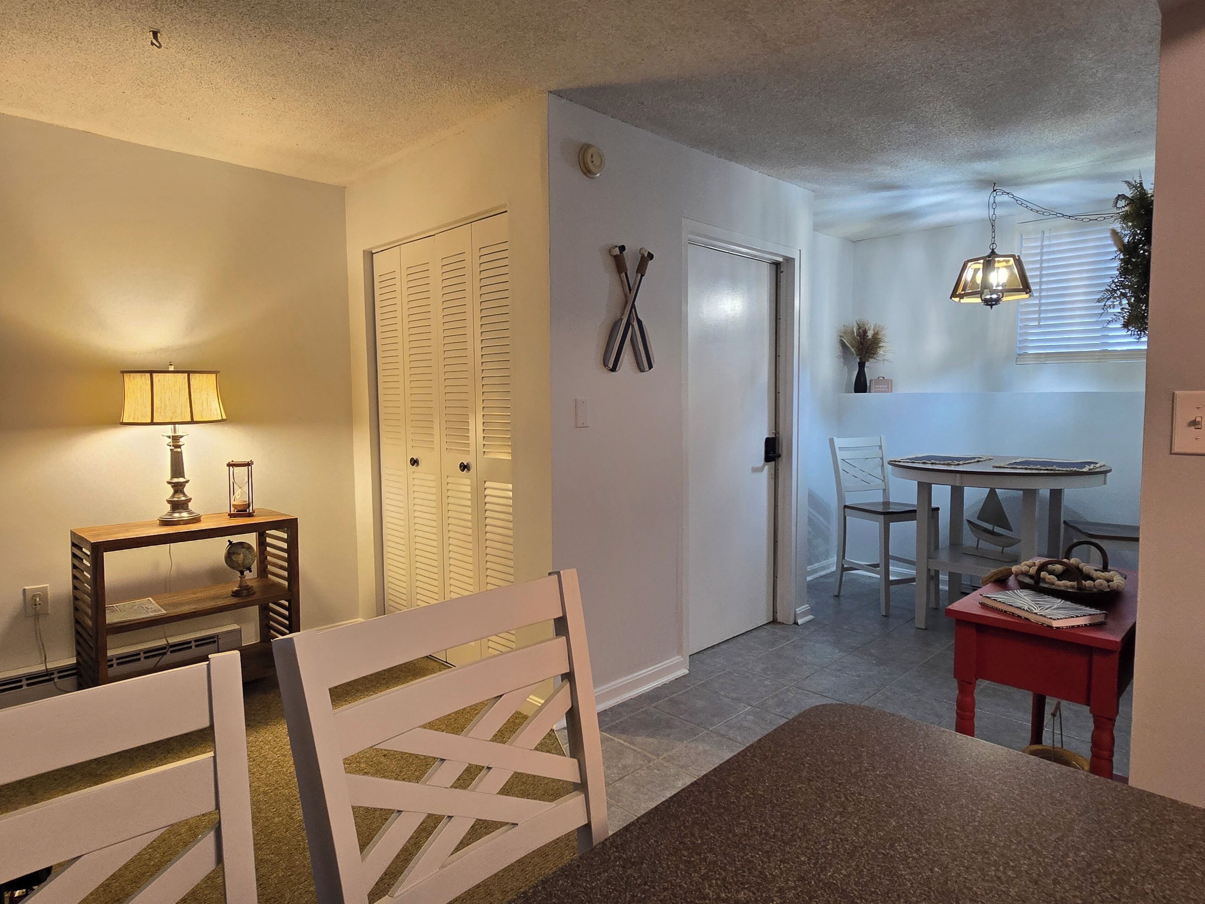 A dining area with a table, chairs, and a lamp. There is a door leading to another room.