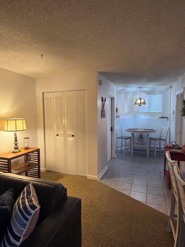 A living room with a couch, a table with a lamp, and a closed white closet.