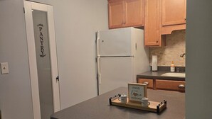 A kitchen with wooden cabinets, a white refrigerator, and a small island with a wooden tray holding salt and pepper shakers. - Weirs beach retreat (Laconia)