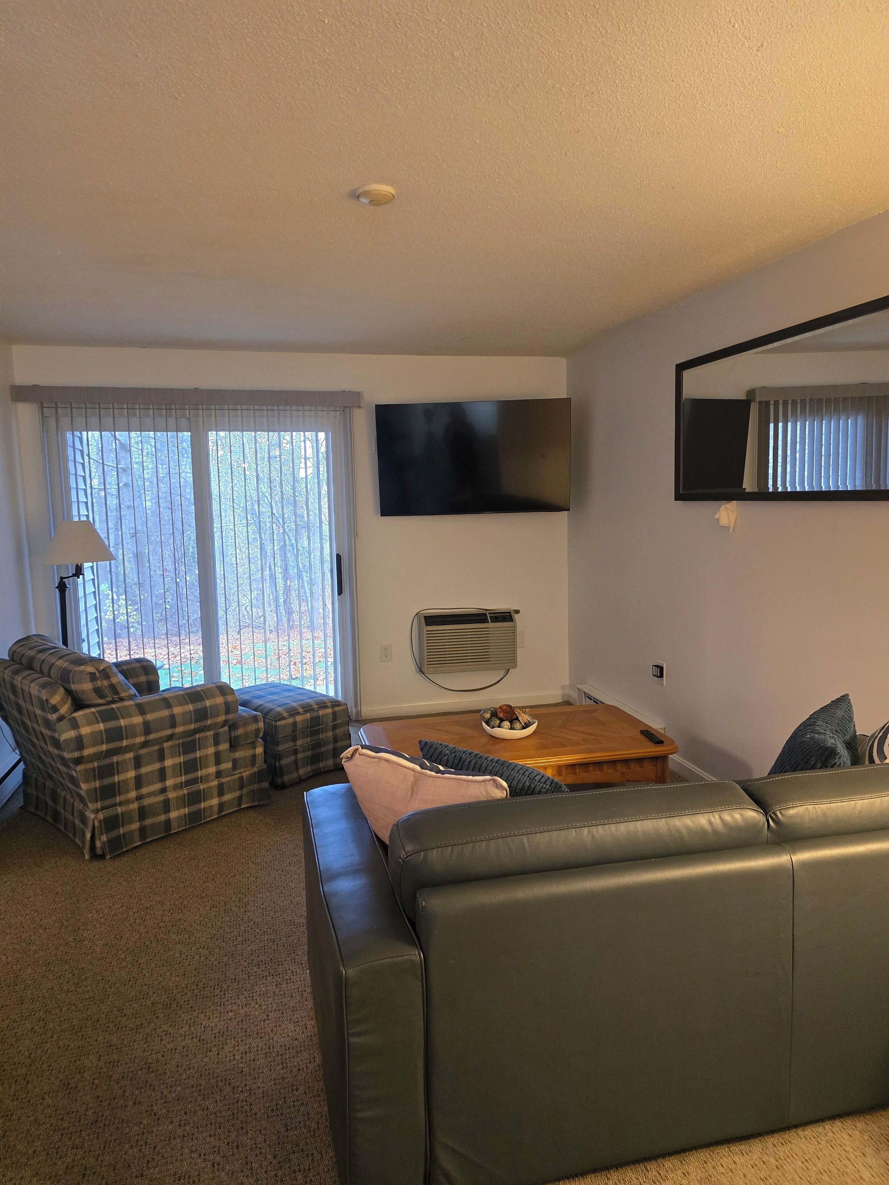 A living room with a sofa, a coffee table, and a television mounted on the wall.