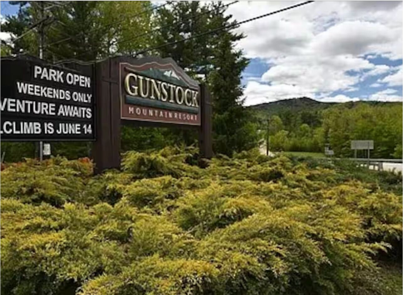 Een bord voor Gunstock Mountain Resort met tekst die aangeeft dat het park in het weekend open is en dat er een klimevenement plaatsvindt op 14 juni.