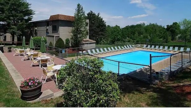 A swimming pool with lounge chairs and umbrellas, surrounded by a fence and greenery. - Weirs beach retreat (Laconia)