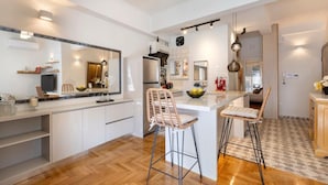 A modern kitchen with white cabinetry, a central island with stools, and a large mirror above the island. - S P ART Boutique Acropolis (Athina)