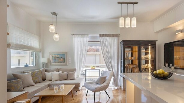 A modern living room with a sofa, a coffee table, and a chair. There is a kitchen area with cabinets and a dining table. - S P ART Boutique Acropolis (Athina)