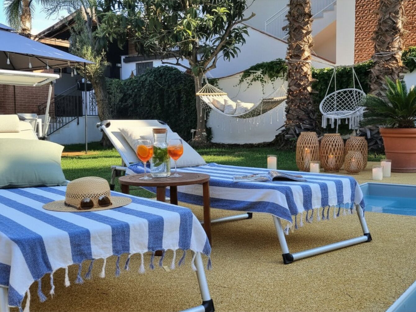 Two lounge chairs with striped covers, a small table with drinks and a hat, and a hammock.
