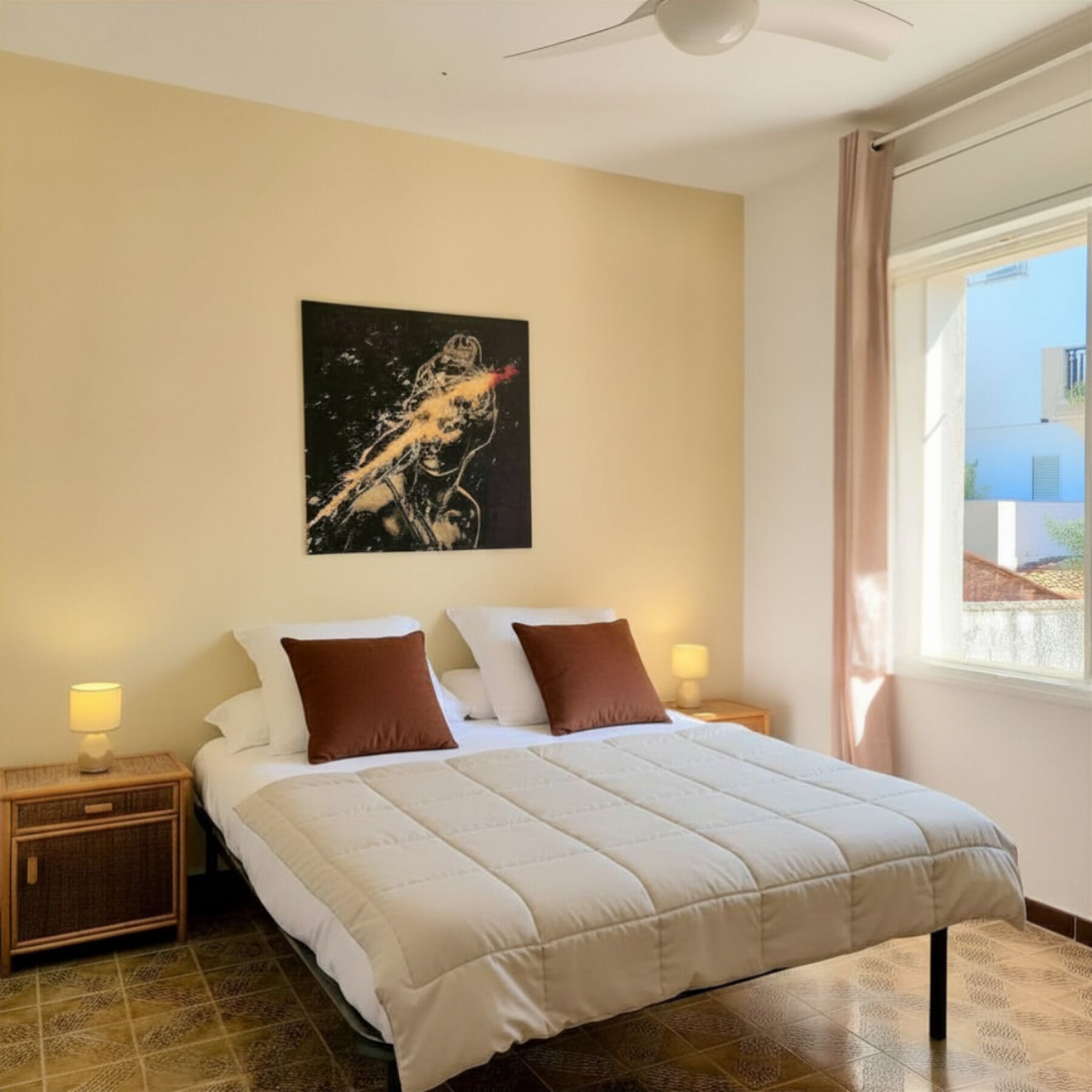 A bedroom with a bed, two nightstands, a ceiling fan, a window with curtains, and a wall-mounted painting.