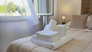 A neatly made bed with folded white towels, a bedside lamp, and a window with curtains. - VFH The Sicilian Dream Pool Villa (Altavilla Milicia)