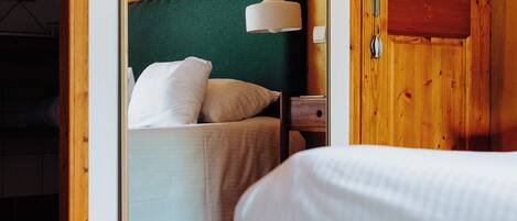 A bedroom with a wooden door, a bed with white bedding, a green upholstered headboard, and a hanging light fixture.