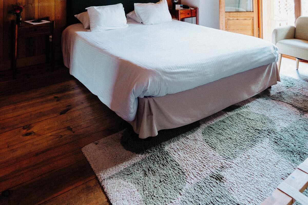 Une chambre aux murs lambrissés, avec un grand lit, une table de chevet, une chaise et une fenêtre donnant sur un beau paysage.