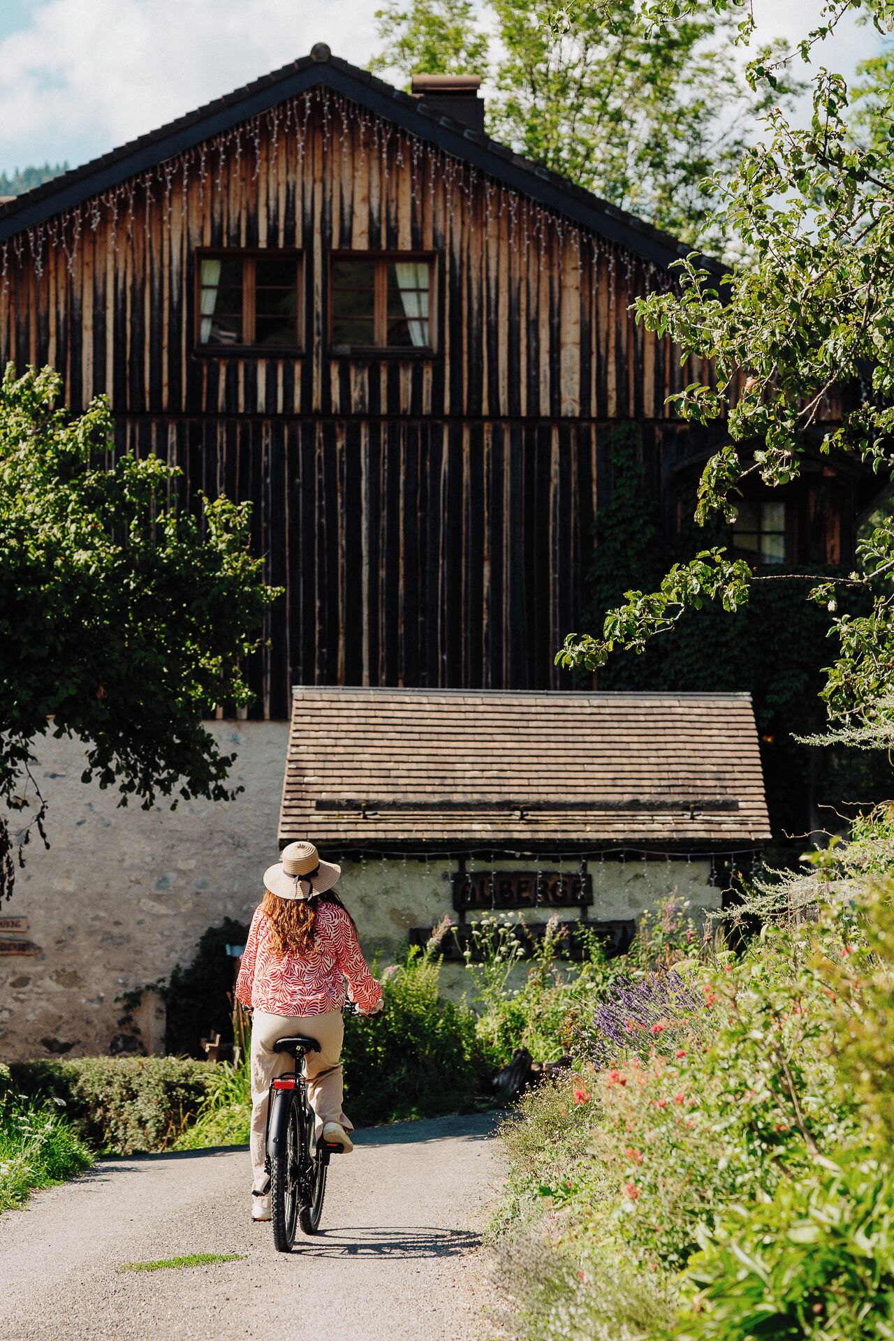 A rustic wooden building with a dirt path leading to it, surrounded by greenery.