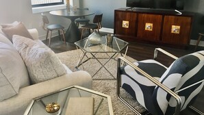 Ein Wohnzimmer mit Sofa, Sessel, Couchtisch, Fernseher und einem Essbereich mit Stühlen und Tisch.