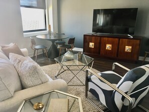 A living room with a sofa, armchair, coffee table, TV, and a dining area with chairs and a table. - Available for World Cup (Kansas City)