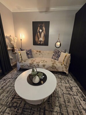A living room with a white sofa, a round coffee table with a vase and a card, a horse painting on the wall, and a floor lamp. - Cozy Tempe Condo King Bed, Pool & Gym Near ASU & Sonoran University Medical (Tempe)