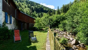 Un edificio rústico con fachada de madera, un patio cubierto de césped y un arroyo.