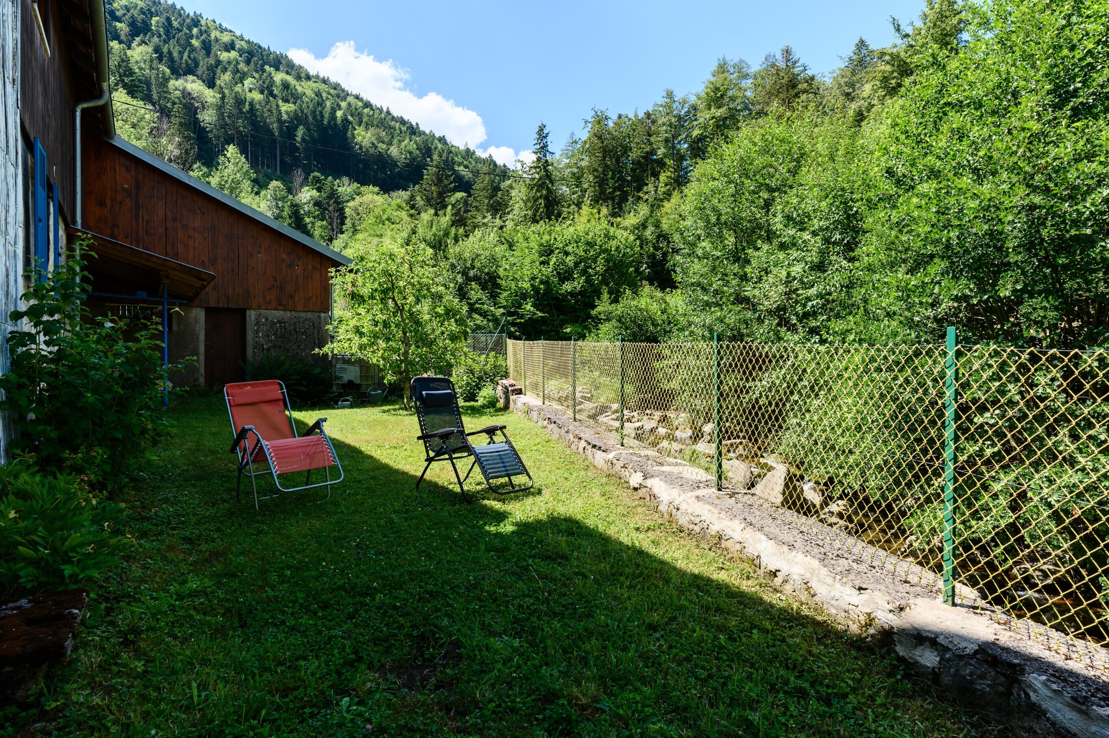 Un espace extérieur clos, agrémenté de deux chaises longues, d’une construction en bois et dominé par un paysage montagneux.