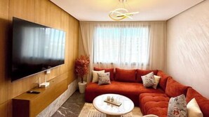 Un salon moderne avec un téléviseur à écran plat fixé à un mur en bois, un canapé rouge agrémenté de coussins, une table basse et un luminaire au plafond au design original.