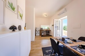 A modern kitchen with a dining area, wooden flooring, and a view through the open door.