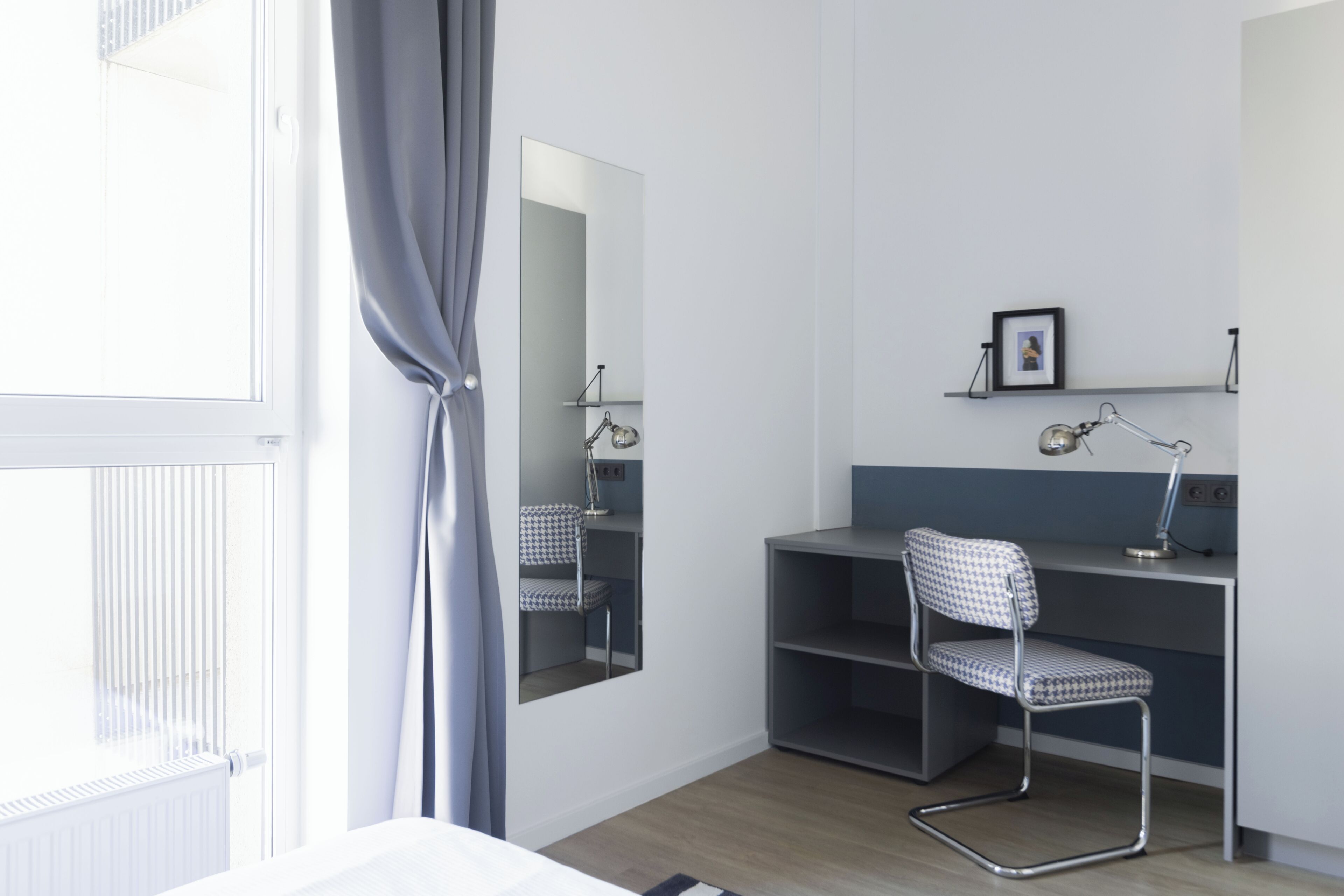 A room with a desk, chair, mirror, and radiator.