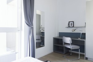 A room with a desk, chair, mirror, and radiator.