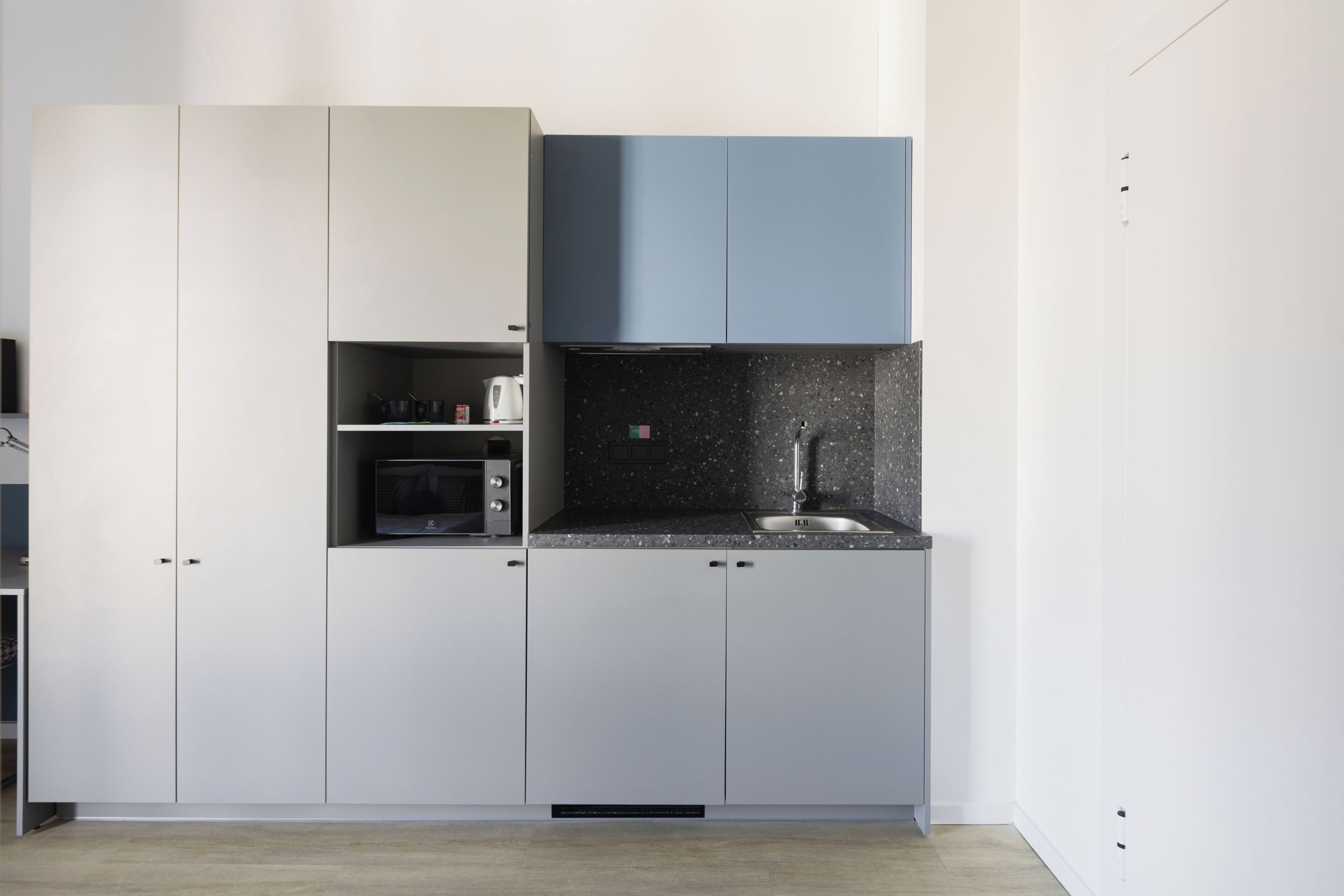 A modern kitchen with white and blue cabinets, a black countertop, and a stainless steel sink.