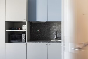 Una cocina compacta con microondas, un lavamanos y un salpicadero negro con motas.