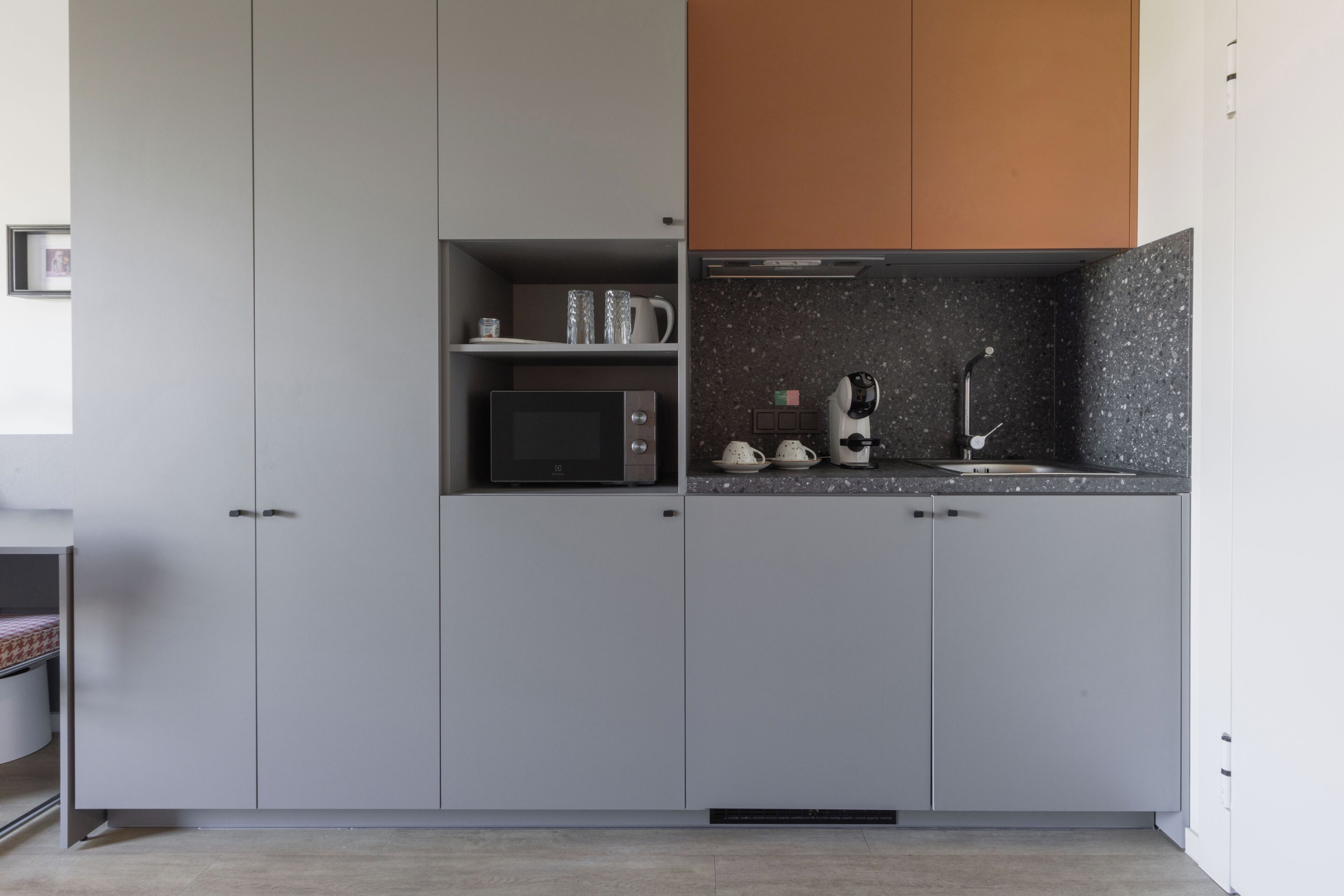 A modern kitchen with grey cabinets, a microwave, a coffee machine, and a granite countertop.