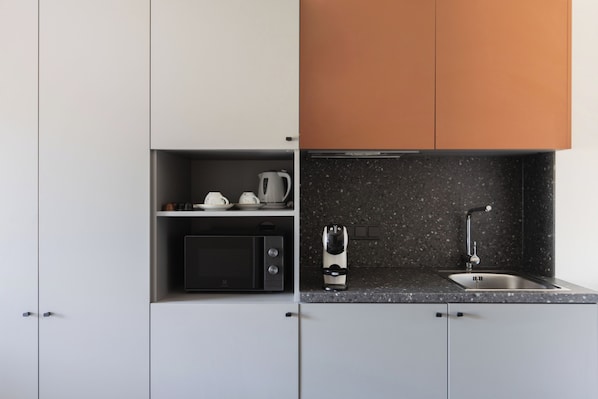 Una cocina moderna con armarios blancos, un microondas negro, una cafetera y un lavamanos con salpicadero moteado.