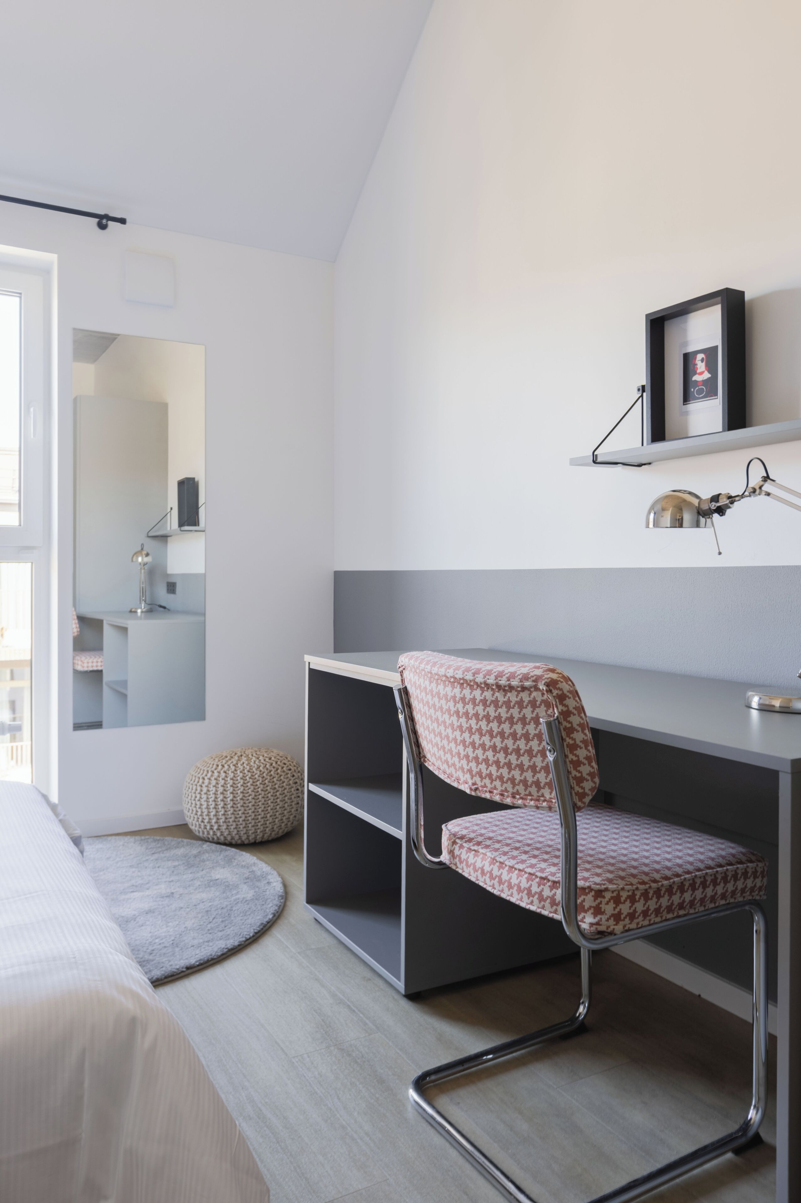 Un dormitorio moderno con cama, escritorio con silla, espejo y estante con lámpara.