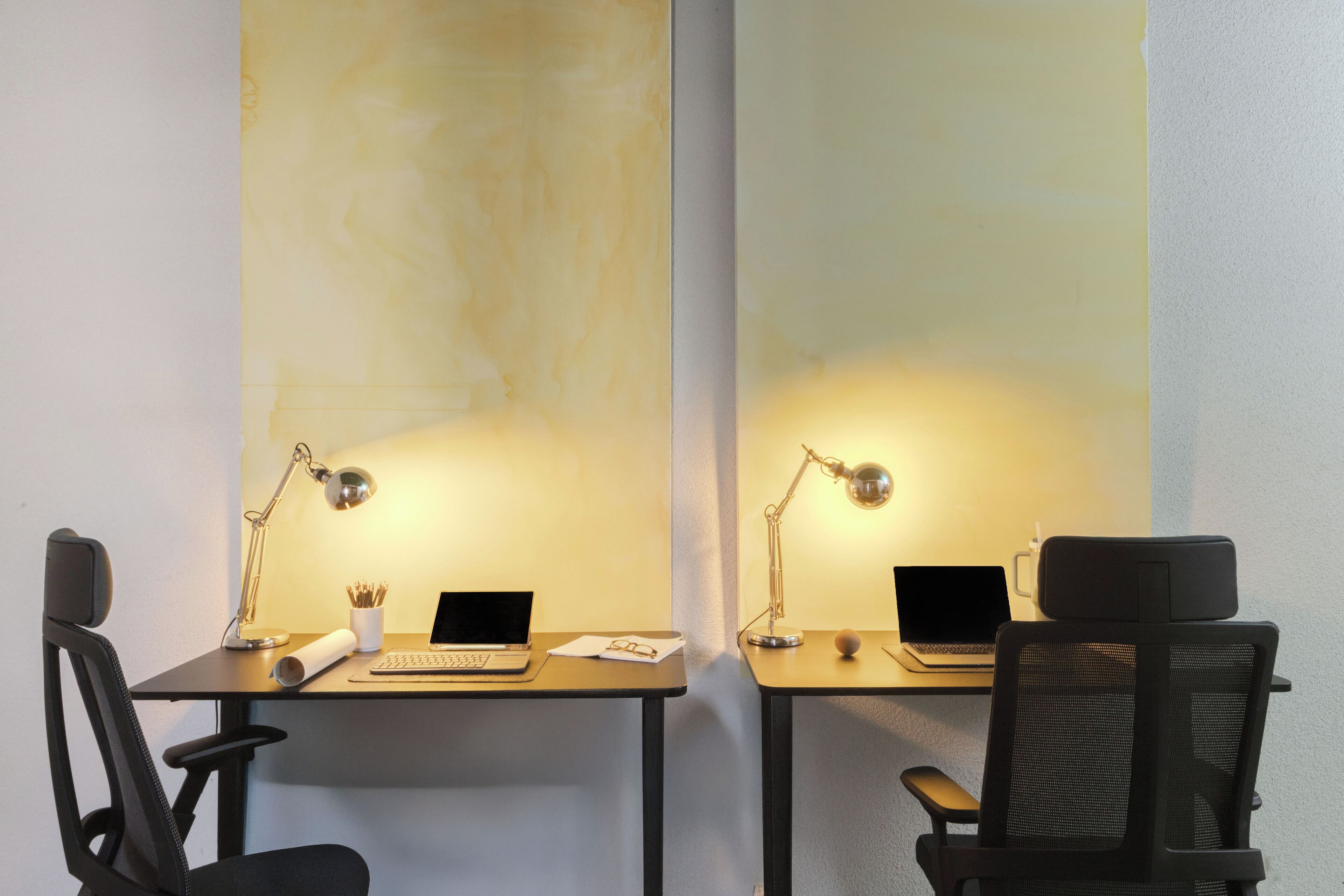 Zwei Schreibtische mit Laptops, jeweils mit einer Schreibtischlampe, einer Tasse und einer Brille.