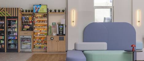 Un espacio comercial moderno y bien iluminado, con zona de estar, mostrador refrigerado y varias estanterías con productos.