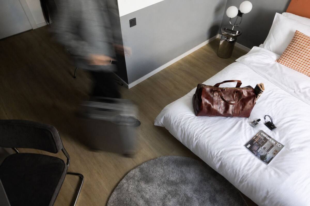A hotel room with a bed, a suitcase, a handbag, and a magazine on the bed.