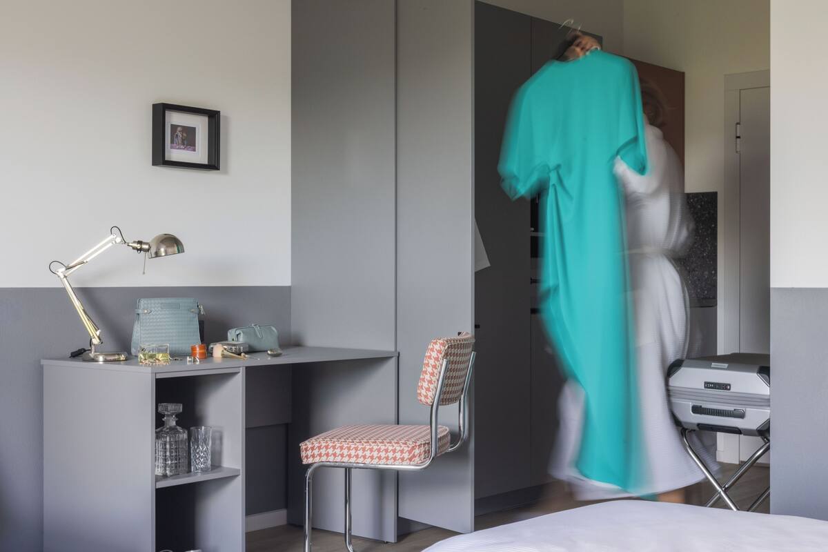 A modern hotel room with a desk, chair, and a bed.