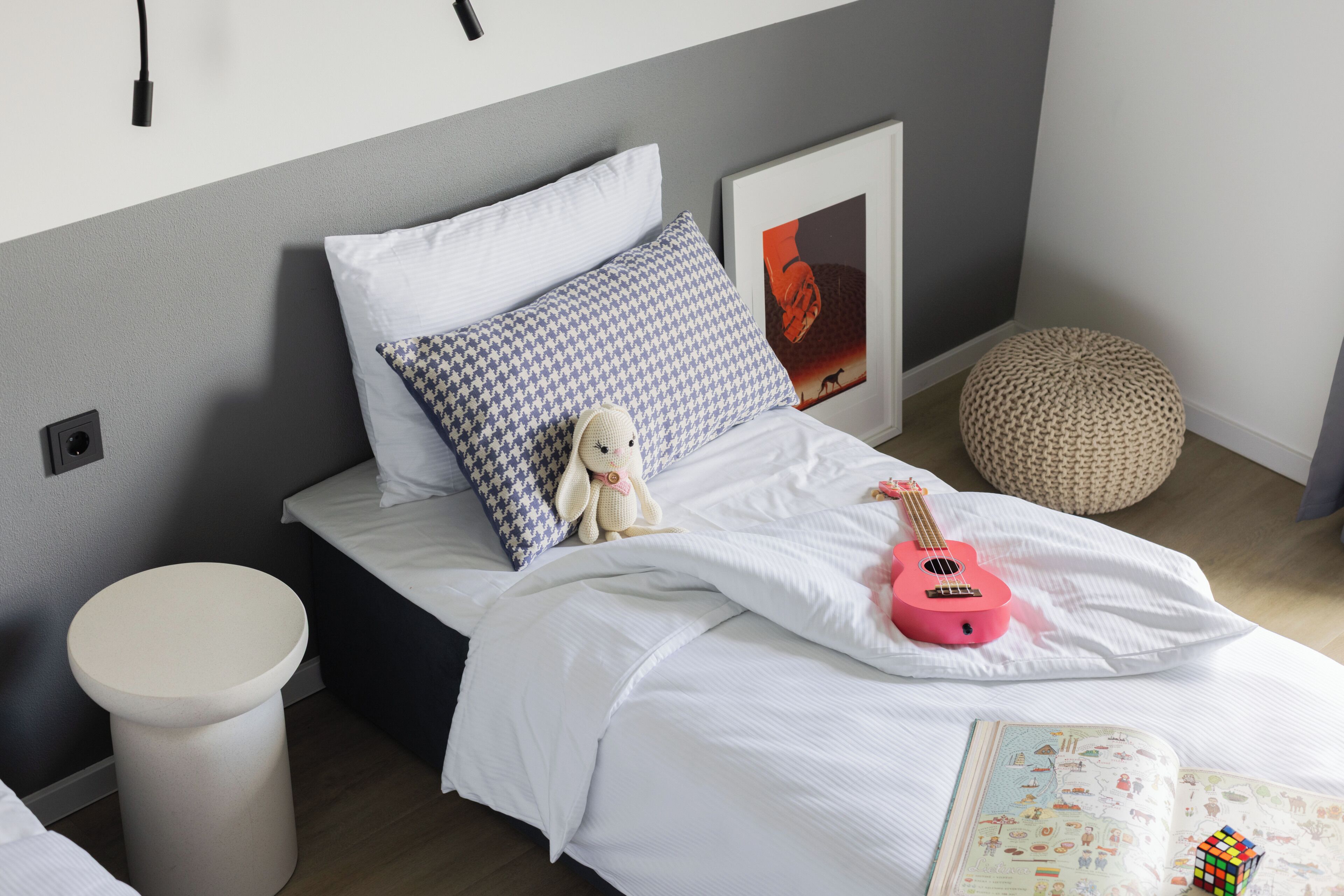 A neatly made bed with a pink guitar, a plush toy, and a framed picture on the headboard.