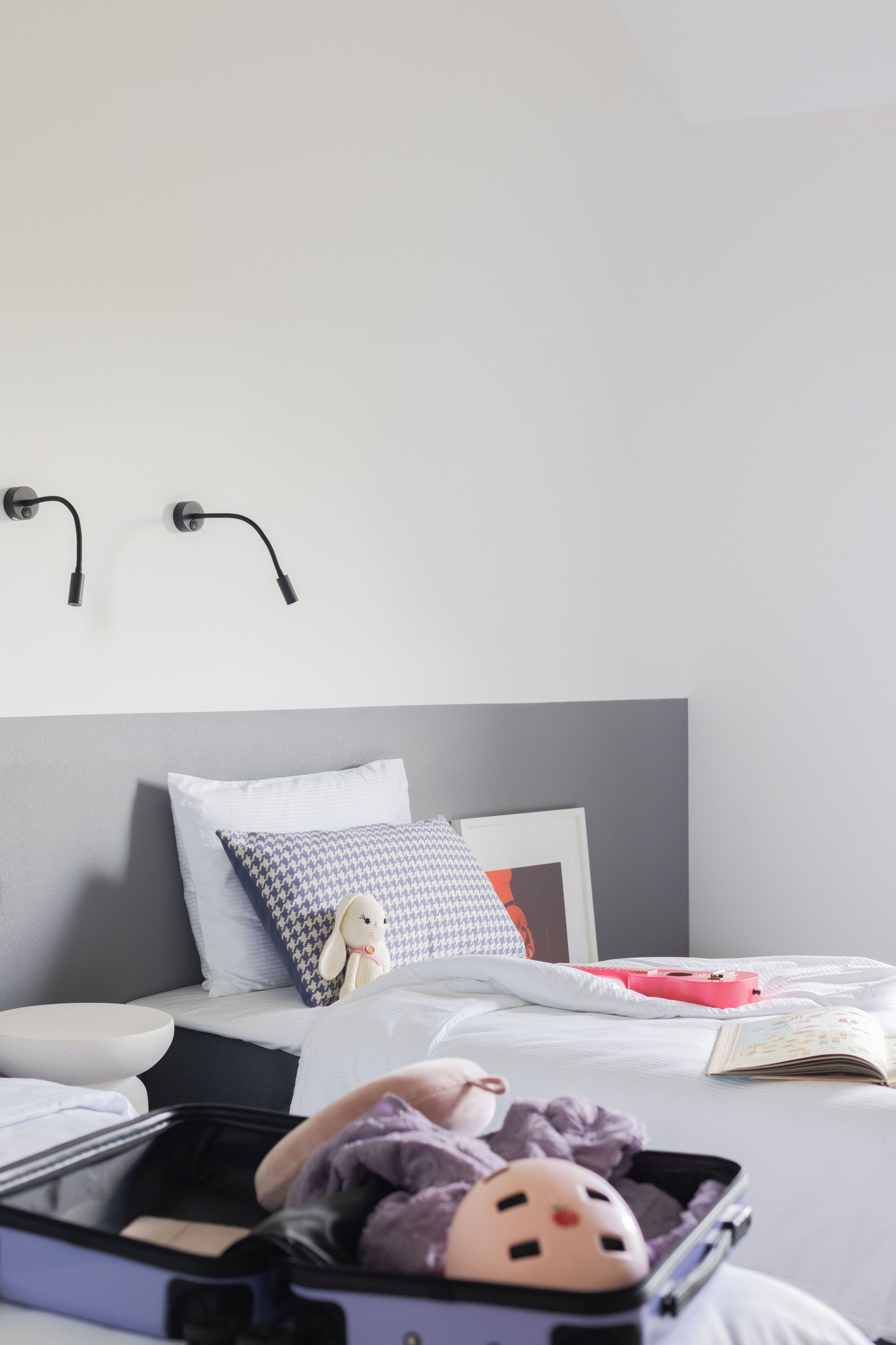 A neatly made bed with pillows, a bedside table, a suitcase, and a stuffed toy on the bed.